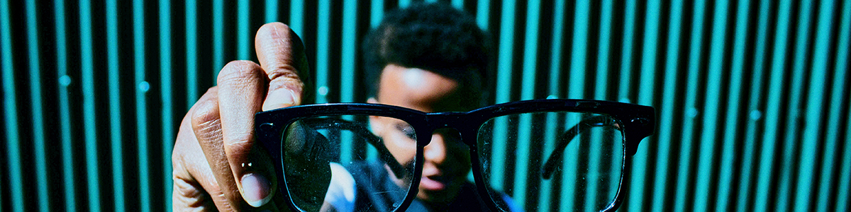 A person holds eyeglasses up to the camera 1200x300 banner press release.jpg